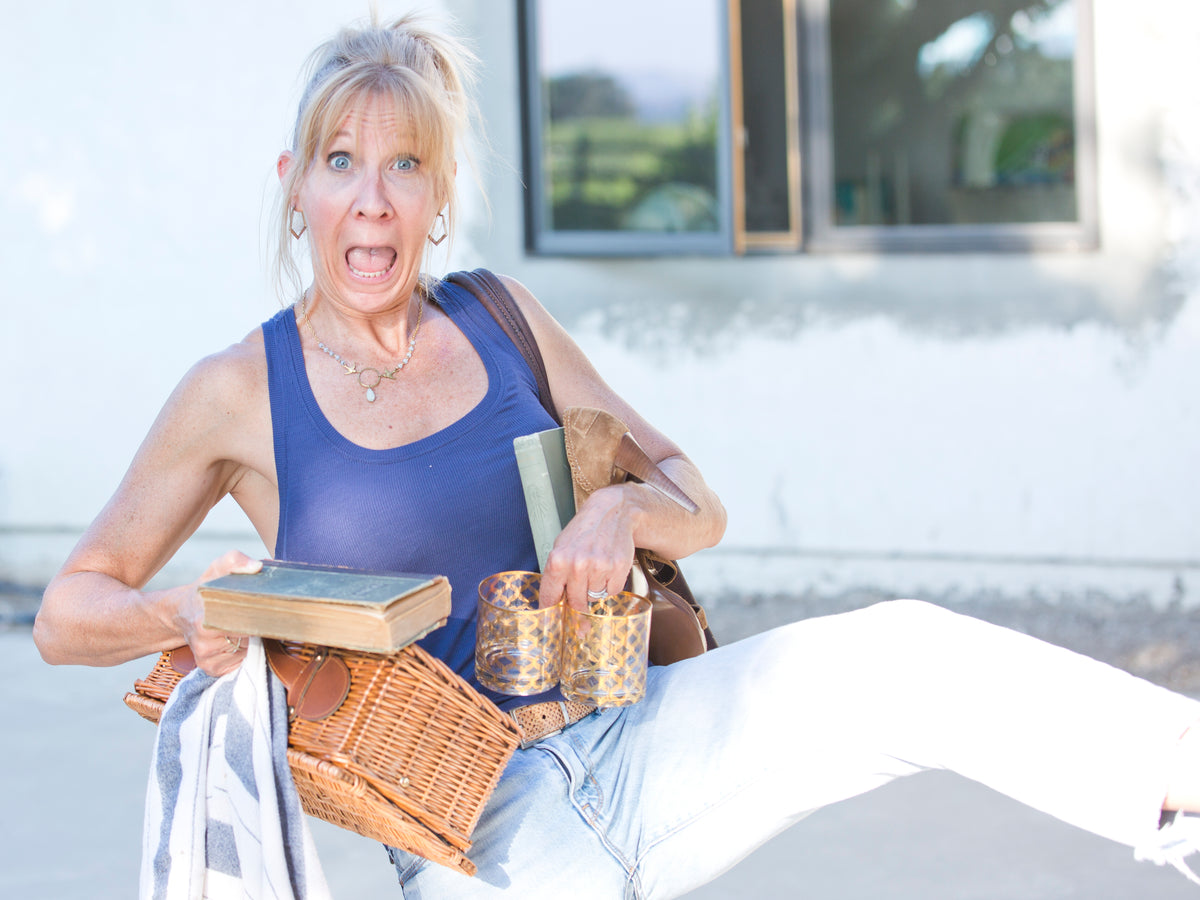 Santa Barbara California personal stylist, Paula Parisotto, juggles a wristlet, antique book, picnic basket, blanket and glasses while making a funny face. 