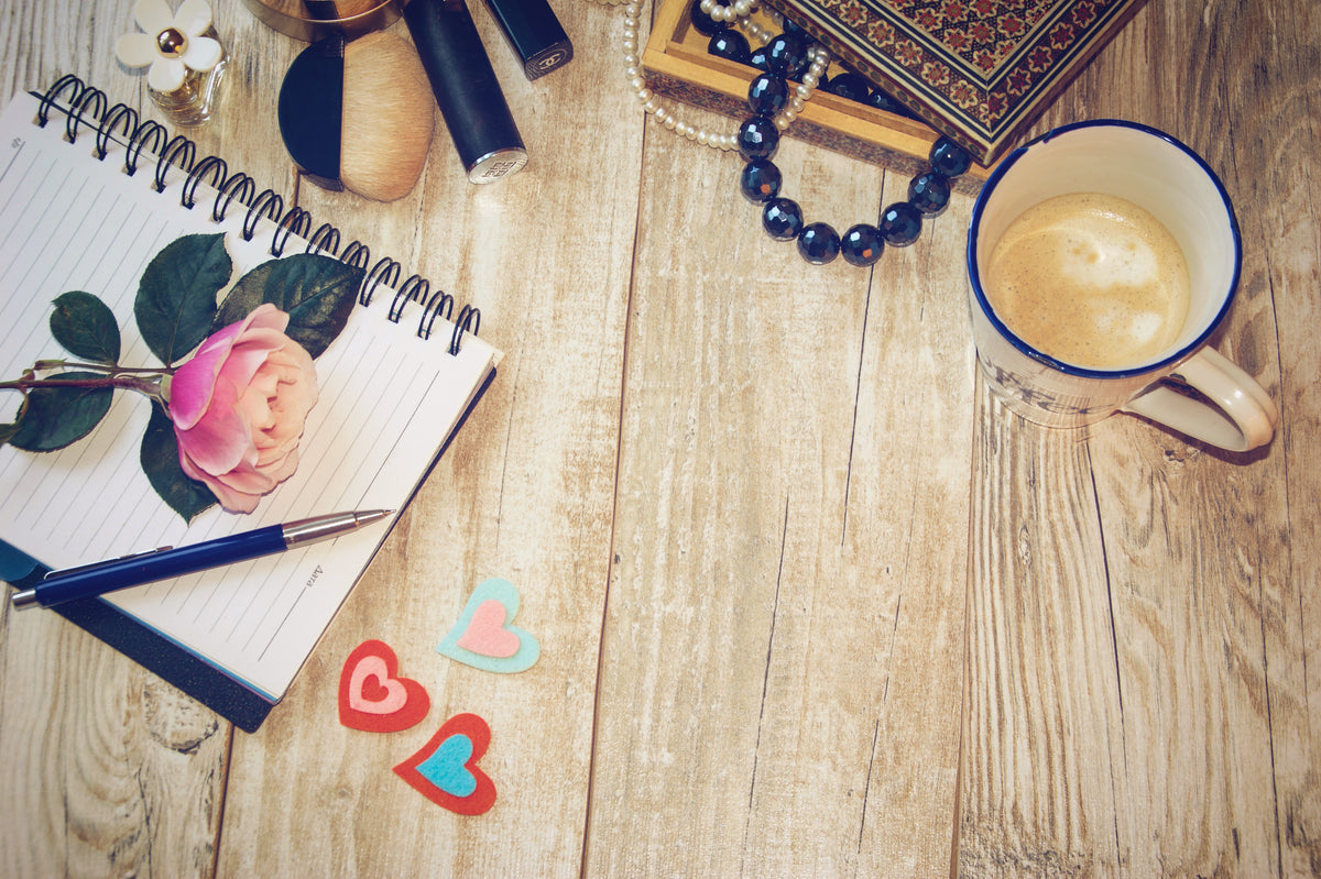 View of a wooden table from above with a cup of coffee, jewelry, pen and journal with tips for accessorizing your look 