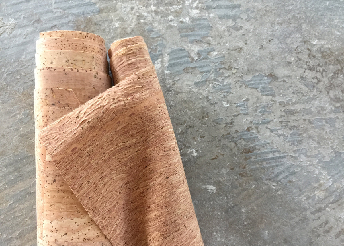A roll of natural cork fabric sits on top of cement table top. 
