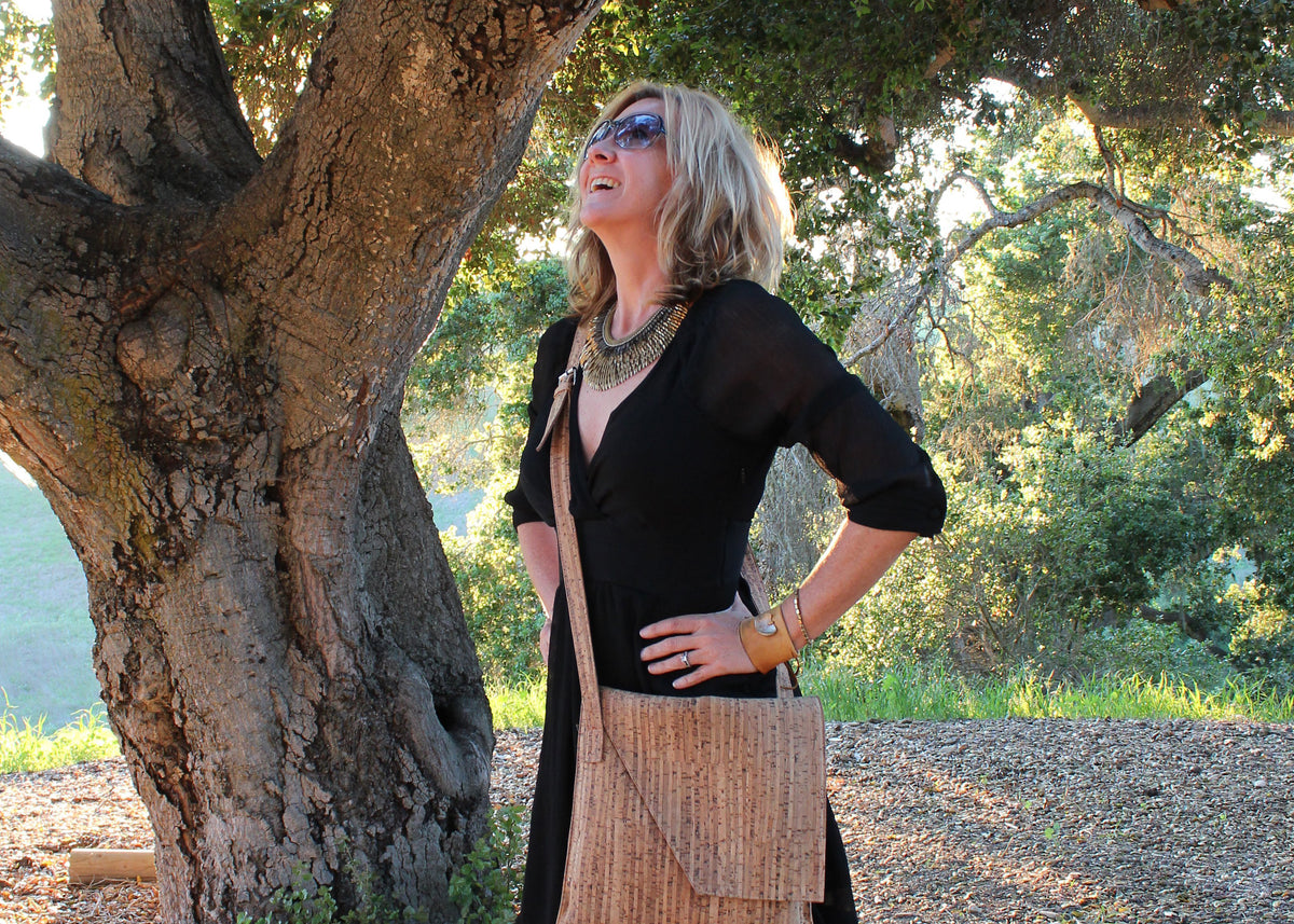 California cork purse designer Paula Parisotto, proudly stands underneath a large oak tree waring a black dress, sunglasses and cork crossbody bag.