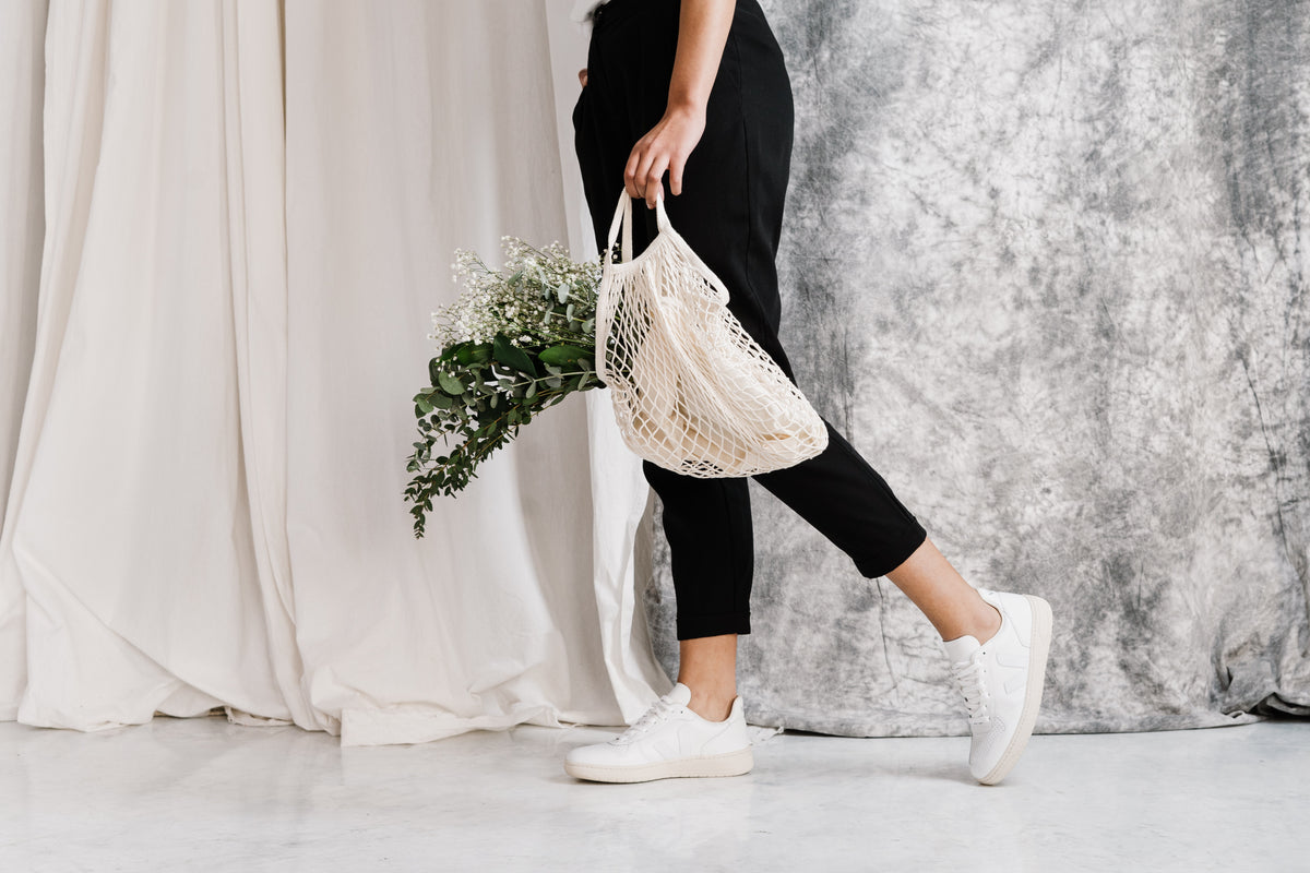 a lady wearing a slow and sustainable fashion brand carrying a woven grocery bag full of greens 